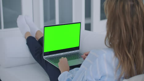 A-young-woman-sits-with-a-laptop-on-her-lap-with-a-green-screen-during-quarantine.-chromakey-on-the-laptop-screen.-Make-a-video-conference-and-talk-to-the-green-screen